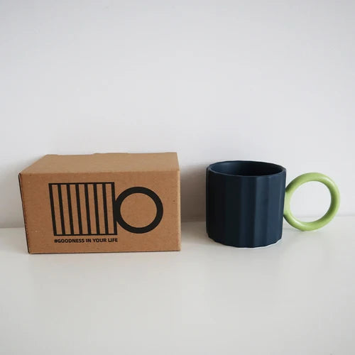 BLUE MUG WITH A GREEN BIG CIRCLE HANDLE AND A BOX